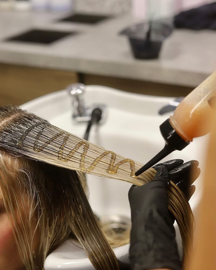 Toner worked through a sectioned strand of blonde hair at the shampoo bowl