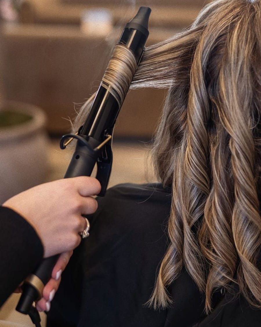 A section of highlighted hair wrapped around a curling iron mid-style
